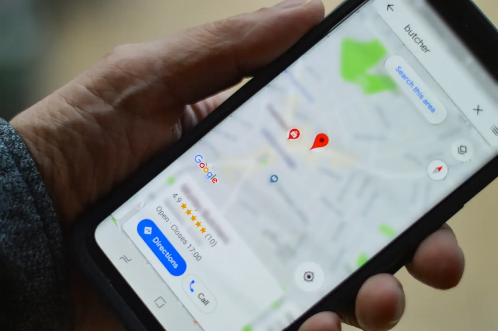 A hand holding a phone showing Google Maps, with a local business's Business Profile listing its rating, opening hours and Directions and Call buttons